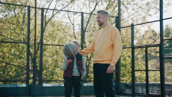 Dad Puts His Arm Around His Son While Talking at Basketball Court on a Sunny Day