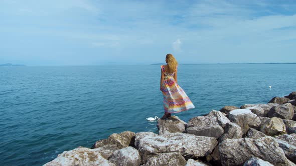 Girl in a Dress on Stones Looking at the Ocean