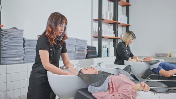 Asian woman customer lying down on salon washing bed getting hair washed in hair salon by stylist