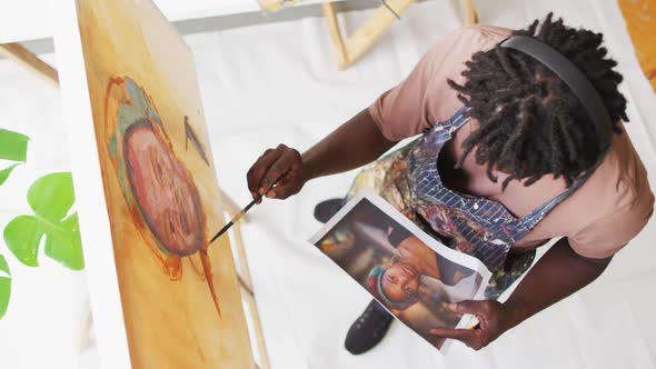 Overhead view of african american male artist painting on canvas looking at photo at art studio