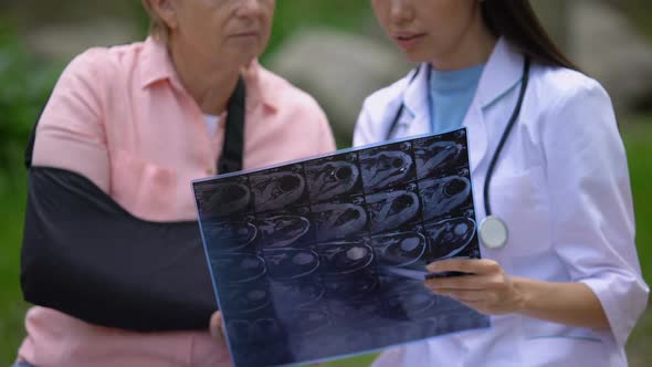 Young Physician Showing X-Ray Image to Mature Female Patient Wearing Arm Sling