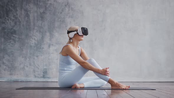 Young and sporty girl in sportswear is doing exercises at home using virtual reality helmet.