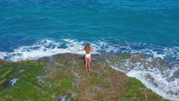 Aerial View. Sexy Girl Standing on the Cliff on the Rocky Beach. A Woman Looks Into the Distance.