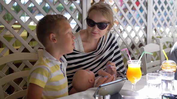 Woman with baby and elder child in cafe on summer day