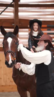 Senior Man Assisting Granddaughter Horseback Riding in Ranch