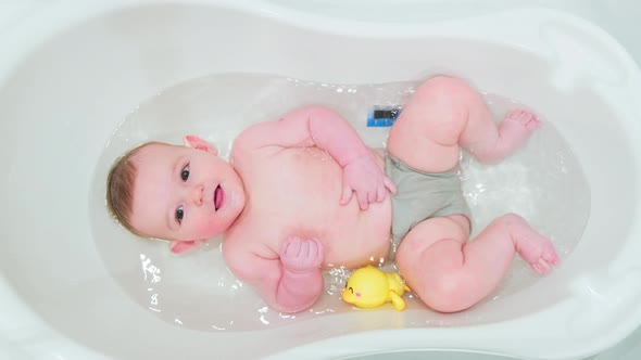 Infant baby plays with toys while lying in a children bath