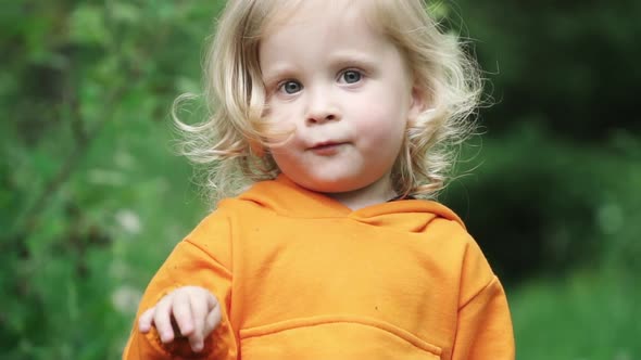 Little Boy in Bright Orange Hoodie Looks Into Camera and Smiles