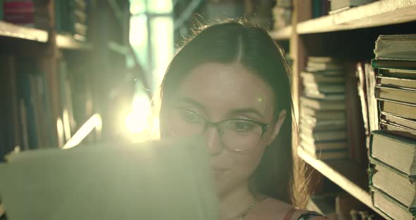 Girl in Glasses Admires of the Book and Flips Through It with Joy in a Library