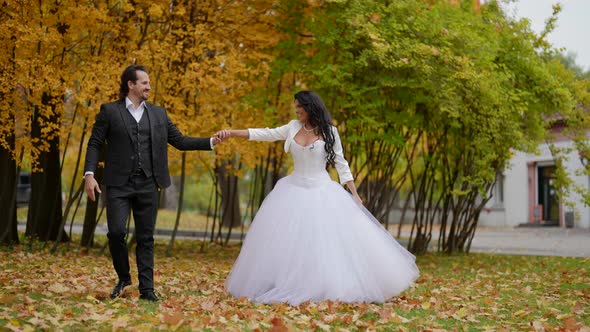 Happy Just Married Couple is Dancing in Park in Autumn Day Joyful Man and Woman in Wedding Gowns