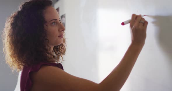 Video of focused caucasian female teacher standing at blackboard and writing