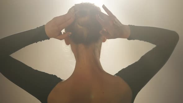 Back View of Slim Young Confident Woman Adjusting Bun Pigtail in Spotlight and Turning to Camera in