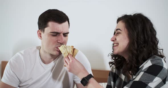 A Happy Couple Man and Woman are Eating Pizza in a Bed at Home