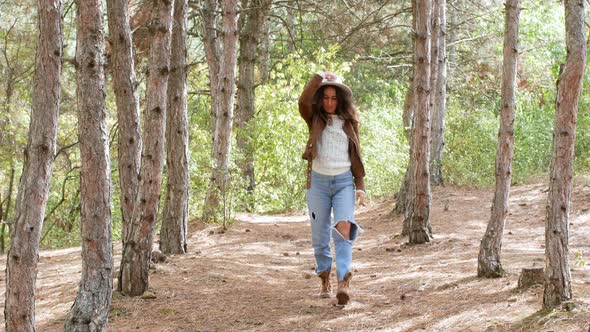 A beautiful young woman in a stylish hat is walking through the woods.