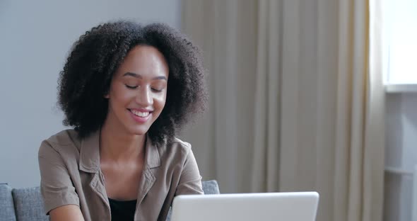 Attractive Young Afro Girl Sitting with Laptop Typing Smiles at Camera Showing Hand OK Sign, Agree