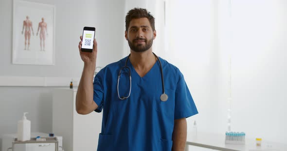 Male Doctor or Nurse Holding Smartphone with Virtual Immunity Passport in Clinic