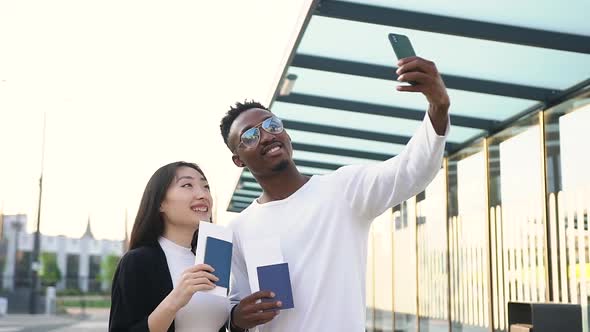 Man and Asian Woman with Long Hair Holding in their Hands Travelling Documents while Making Selfie