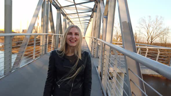 Blonde Girl Walking on the Bridge and Looks Into the Camera at Sunset.