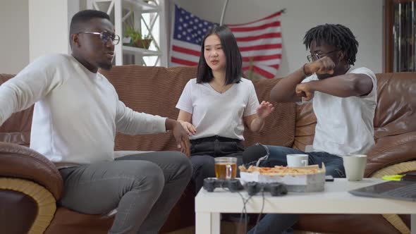 Joyful Multiracial Friends Dancing in Slow Motion Sitting on Couch Indoors