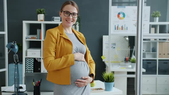 Slow Motion Portrait of Pregnant Girl Employee Standing in Office Room Touching Tummy Smiling