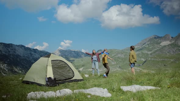 Happy family play with a toy blue plane against tent on background of mountains