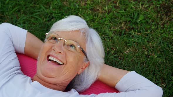 Senior woman lying on exercise mat in garden 4k