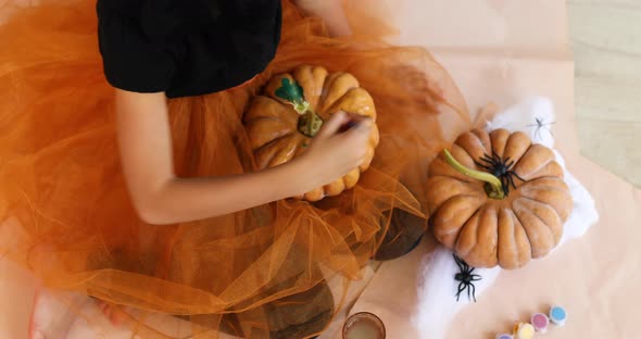 Little girl drawing face on orange Halloween pumpkin