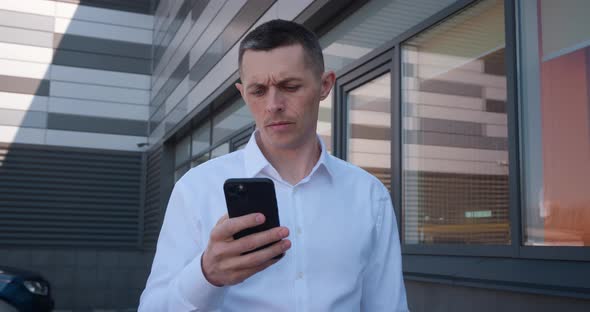 Male Businessman in 40s Wearing White Shirt Texting Message on His Mobile Phone Outdoors Near Office