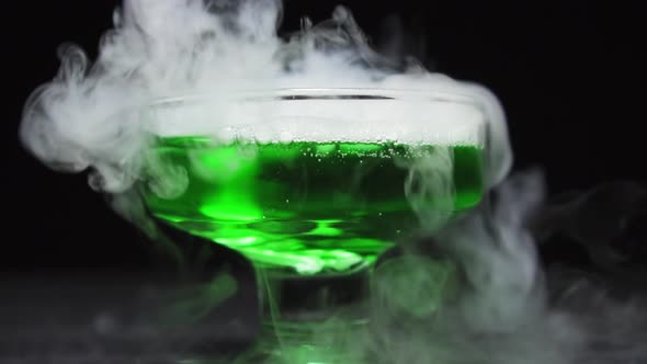 Green Liquid Boils Giving Off Smoke in a Glass Bowl on a Black Background