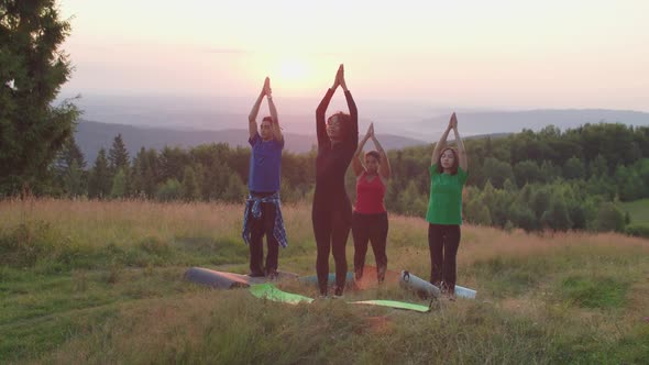 Calm Diverse Multiethnic Sporty Fit People Practicing Group Yoga Class on Mountain Top at Sunrise