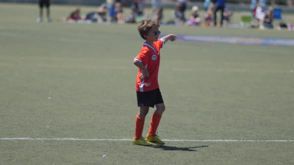 Young boy in orange uniform playing in a youth soccer league game.