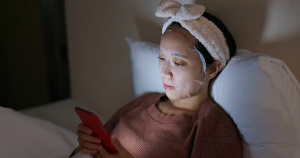 Woman apply paper mask and watch on cellphone at home