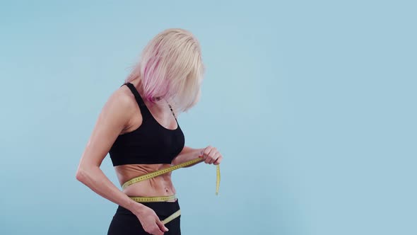 Blonde Woman with a Sports Body Measures the Waist Meter Ribbon in the Studio