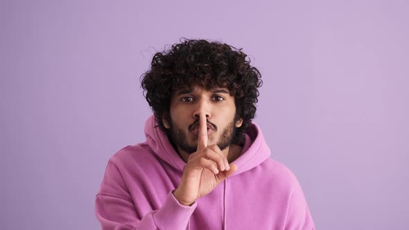 Confident curly-haired Indian man showing silence gesture