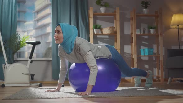 Sporty Muslim Woman is Engaged in Sports Exercises on a Gymnastic Ball at Home