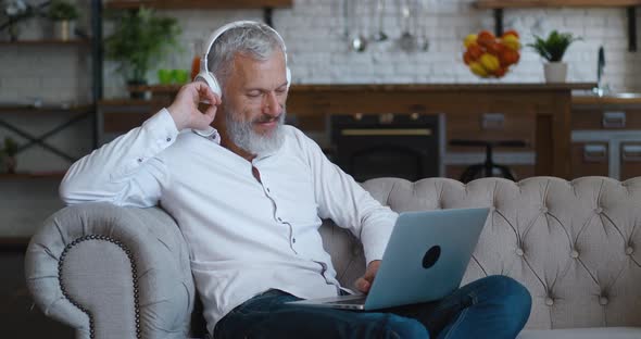 Portrait of Mature Bearded Man with Grey Hair Enjoying Listening Music with Wireless Headphones and