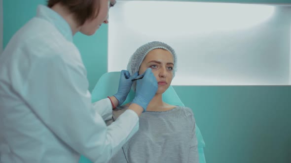 The Beautician in the Office Marks the Client's Face with a Pencil Closeup