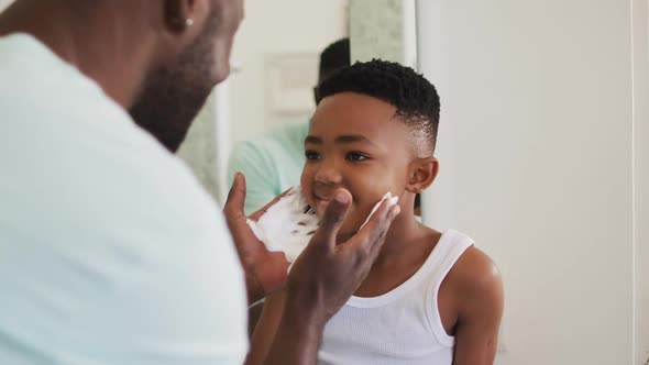 African american father putting shaving cream on his son mouth and laughing together