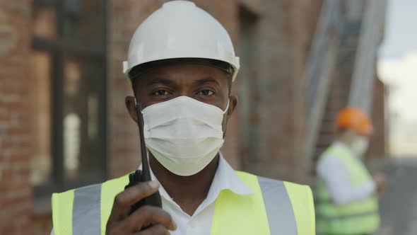 African American Foreman in Mask Using Walkie Talkie Outdoor