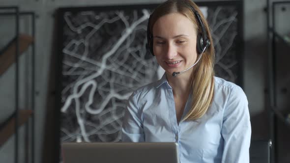 Happy Female Manager Wearing Wireless Headphones, Looking at Laptop Screen, Holding Pleasant