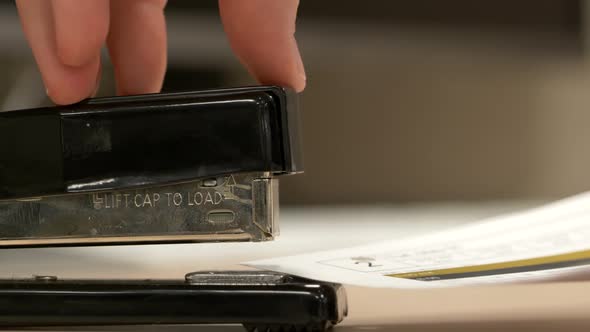 A close up from the side of a black stapler stapling pieces of paper together.