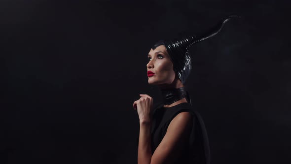 Beautiful woman from a fairytale dressed in black with horns on her head and red lipstick, looking u