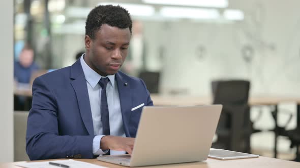 African Businessman Looking at Camera While Working on Laptop