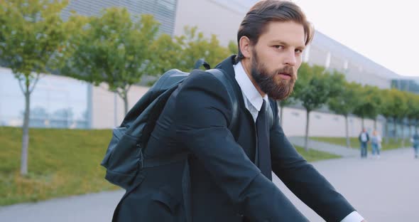 Bearded Man with Backpack which Posing on Camera while Sitting on Bicycle