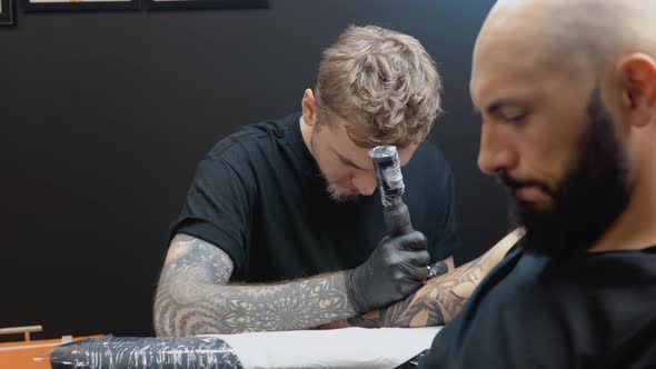 The Client Sits in a Chair While the Tattoo Artist Draws a Picture on His Hand Skin