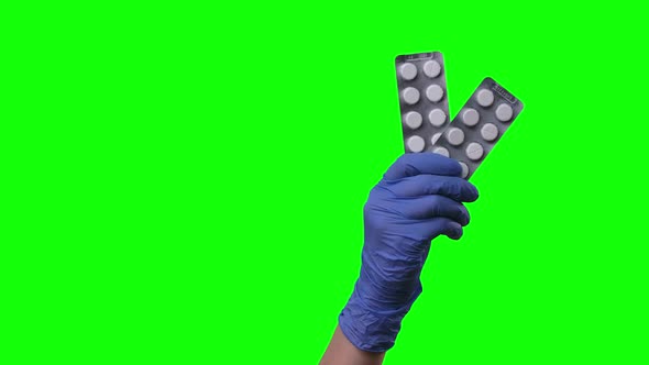 Doctor Shows Pills. Female Hands in Protective Blue Gloves Closeup at Green Screen.