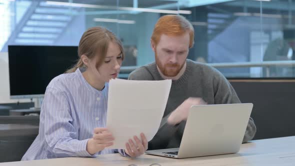 Young Man and Woman Reading Documents While Using Laptop