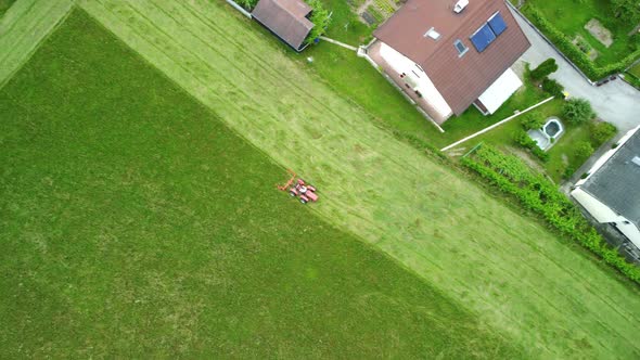Lawnmower tractor cutting grass in straight lines beside urbane settlement. Aerial 4k view.