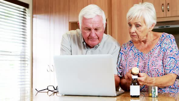 Senior couple checking medicine while using laptop in kitchen