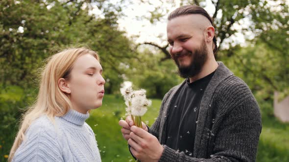 The Man Is Holding a Dandelion Flower and the Woman Is Blowing on It