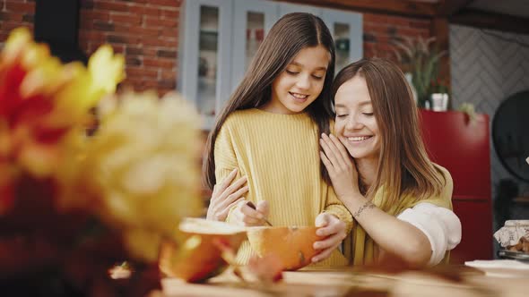 Child Girl Separating Pumpkin Seeds From Pulp with Spoon and Smiling Mum Hugging and Helping Her